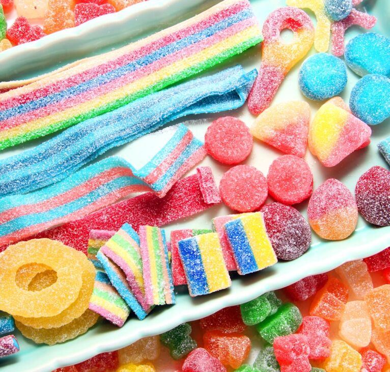 Assorted variety of sour candies includes extreme sour soft fruit chews, keys, tart candy belts and straws. 
Flat lay, sugar background concept for kids birthday party.